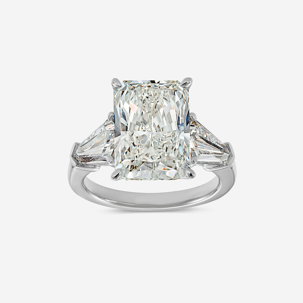 Diamond ring with a central emerald-cut diamond and two smaller triangular diamonds on a white background