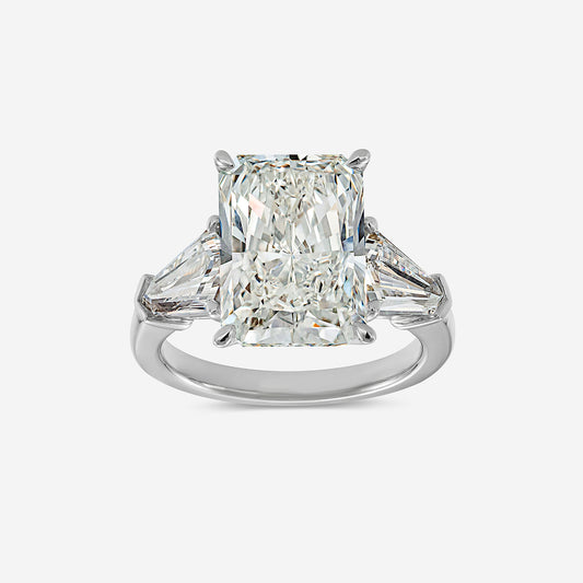 Diamond ring with a central emerald-cut diamond and two smaller triangular diamonds on a white background