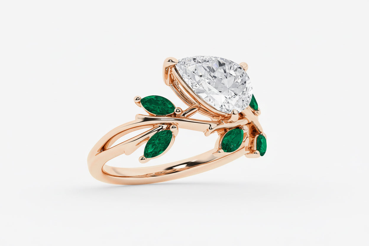 Rose gold ring with a large diamond and smaller emeralds on a white background